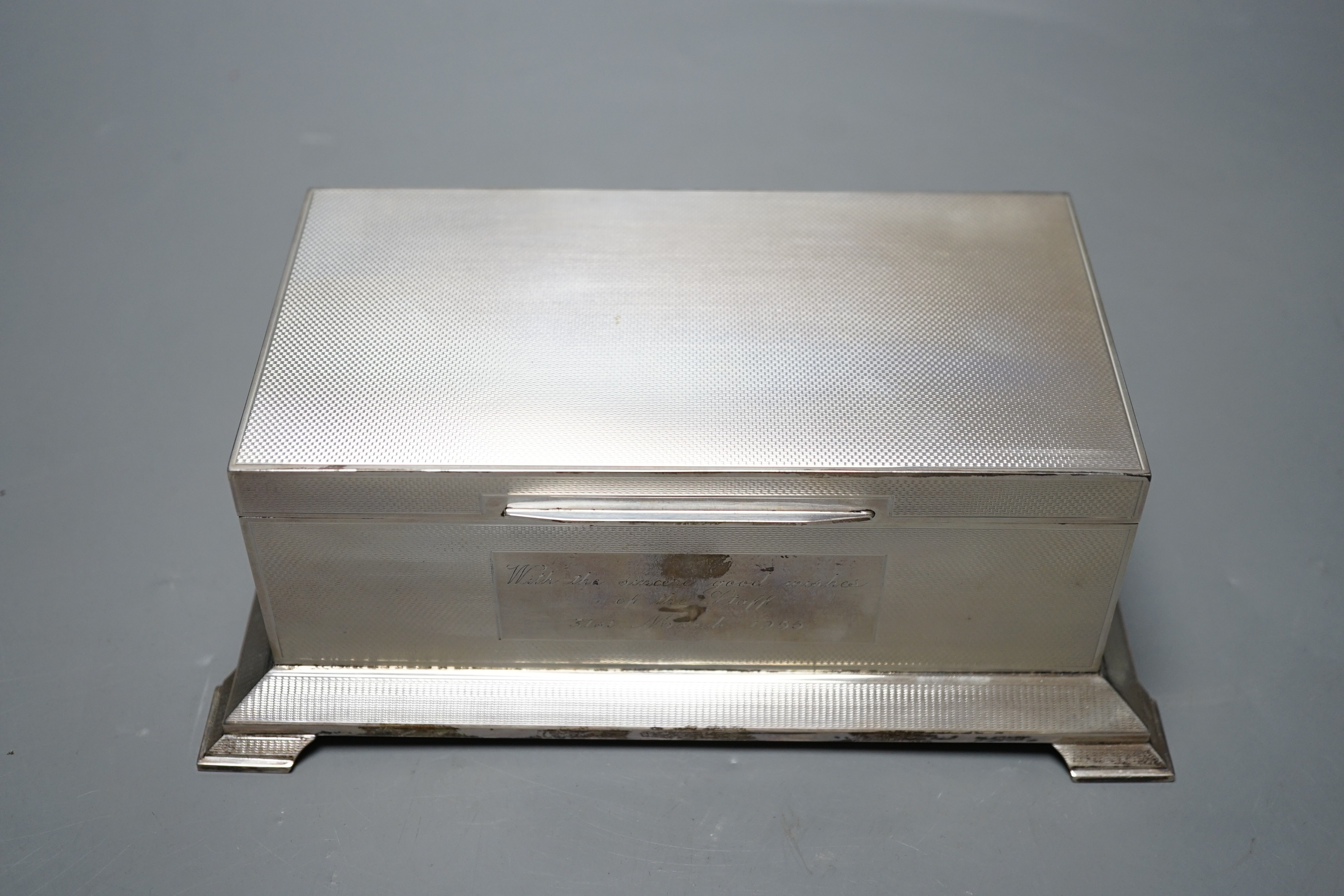 A George VI engine turned silver mounted rectangular cigarette box, Alexander Clark Co Ltd, Birmingham, 1948, with engraved inscription, on bracket feet, 20.4cm.